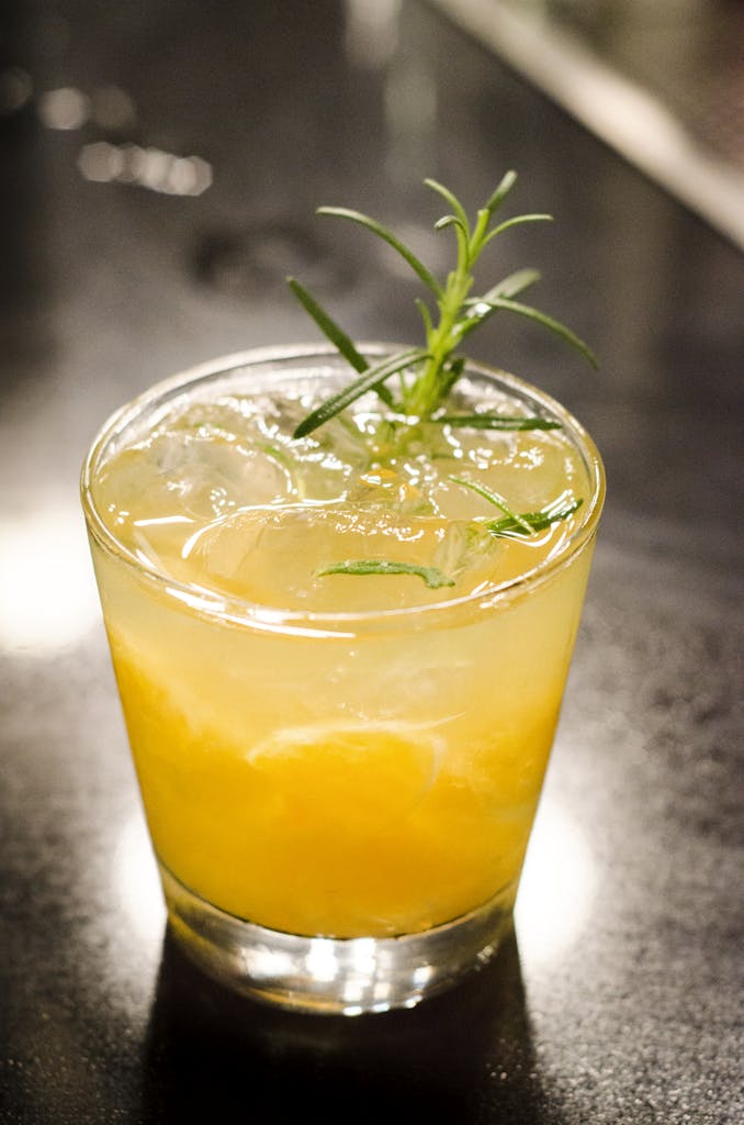 Vibrant citrus cocktail with ice and a green herb garnish, captured indoors.