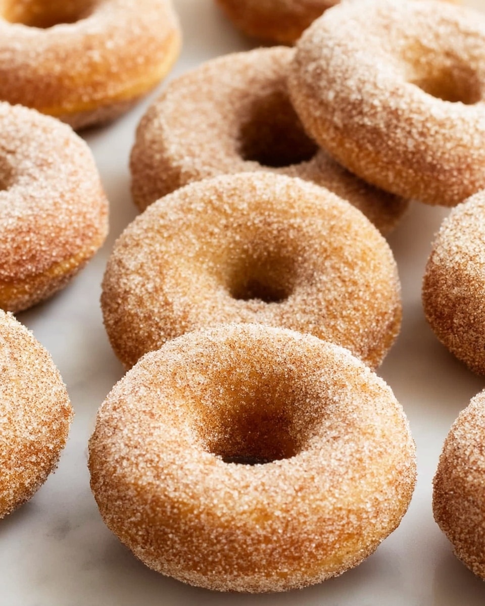 A close-up of several round doughnuts with a hole in the middle, covered evenly with a layer of tiny sugar crystals. The doughnuts have a golden brown color beneath the sugar, showing a soft and slightly rough texture. They are placed directly on a light wooden surface, arranged closely but not touching. The focus is on one doughnut in the front, with others blurred softly in the background. photo taken with an iphone --ar 4:5 --v 7