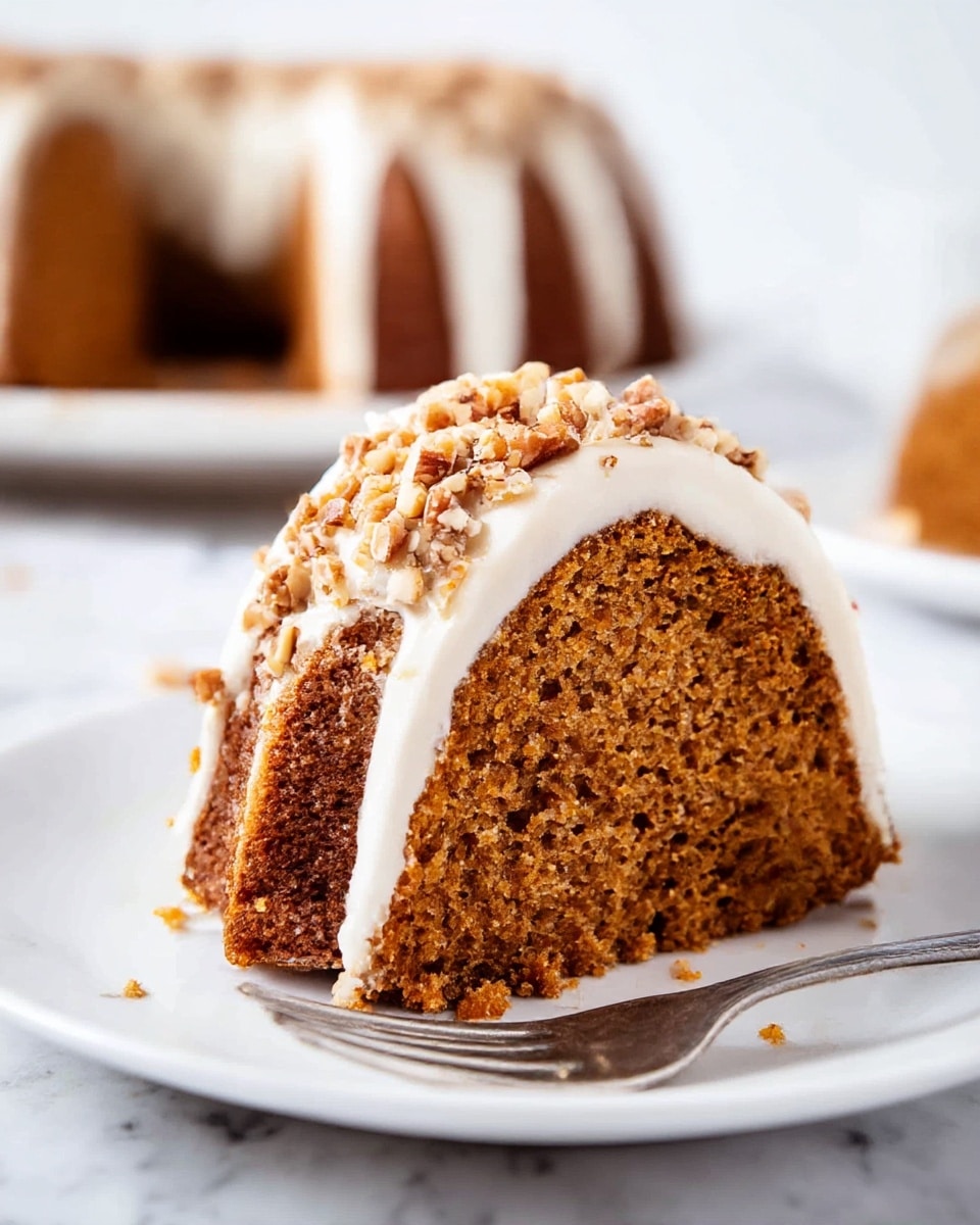 A close-up slice of moist brown bundt cake with a dense texture sits on a white plate with a silver fork resting beside it; the top layer is covered with a smooth white icing that drips slightly over the edge and is sprinkled with chopped nuts, while the background shows another part of the same cake slightly out of focus on a white marbled surface. photo taken with an iphone --ar 4:5 --v 7