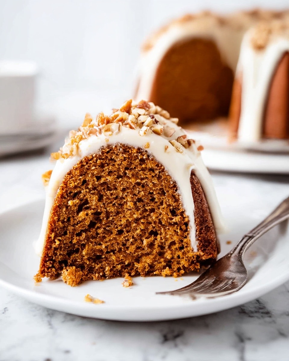 A slice of moist, brown bundt cake is placed on a white plate with a silver fork resting at the base of the slice. The cake has one visible layer with a dense texture and is topped with a smooth, thick white icing that drips slightly down the sides. Small chopped nuts are sprinkled generously over the white icing, adding a rough texture and light brown color contrast. The background shows the remaining bundt cake slightly out of focus on a white marbled surface. The scene is bright and clear, highlighting the cake's rich colors and textures. photo taken with an iphone --ar 4:5 --v 7