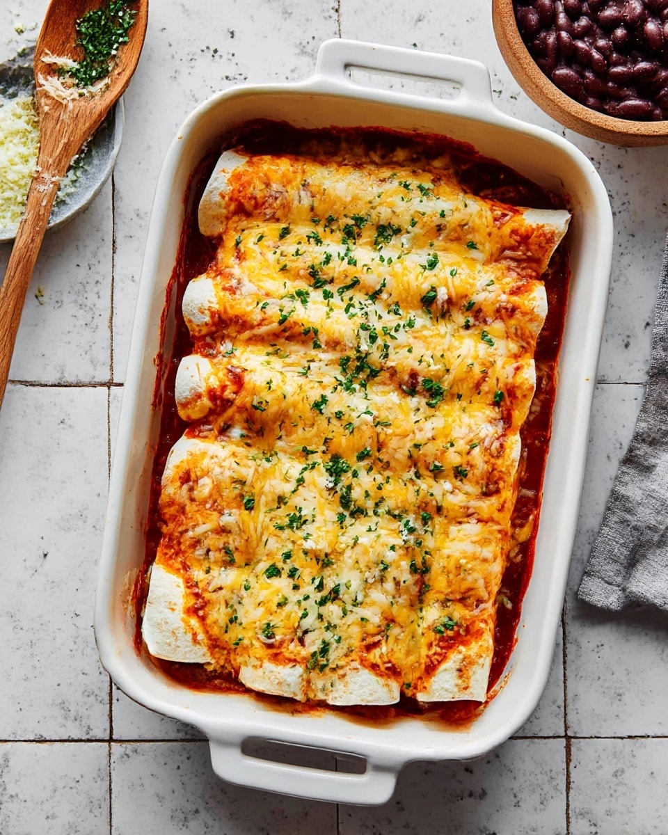 The image shows a white baking dish filled with five rolled enchiladas placed side by side. The enchiladas are covered with a melted layer of yellow and white cheese, sprinkled with chopped green herbs. Underneath the cheese, a red sauce slightly peeks out around the edges of the rolled tortillas, which have a soft and slightly browned texture. The dish is set on a tiled surface with a white marbled texture. Nearby is a wooden spoon with bits of herbs and a bowl containing dark refried beans. Photo taken with an iphone --ar 4:5 --v 7