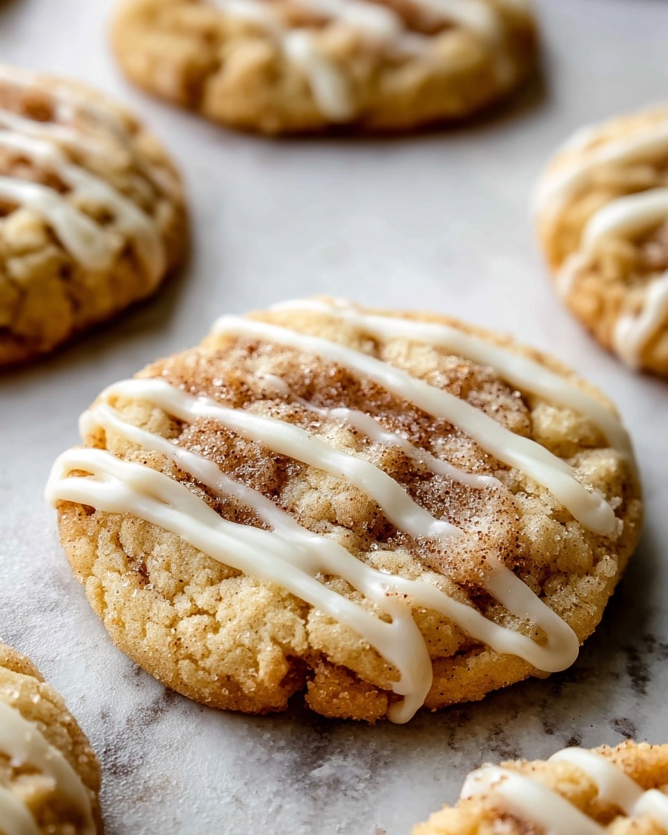 The image shows a close-up of a soft, round cookie on a white marbled textured surface. The cookie has a light golden-brown base with a crumbly texture and a slightly cracked top. There are visible swirls of cinnamon or brown sugar embedded in the center, giving a speckled look with darker brown spots. The cookie is drizzled with three smooth, glossy white icing lines running diagonally across the top. Other similar cookies, slightly out of focus, appear in the background. photo taken with an iphone --ar 4:5 --v 7