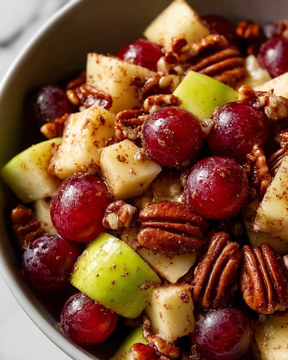 A close-up view of a bowl filled with a fruit and nut mix, featuring deep red grapes, diced pale green and yellow apples, and glossy brown pecans. The pieces are coated lightly with a sprinkle of brown spices, adding a speckled texture on the fruit and nuts. The bowl is white, and it sits on a white marbled surface. The image captures the fresh and natural colors of the ingredients with a slightly shiny coating on some pieces. Photo taken with an iphone --ar 4:5 --v 7