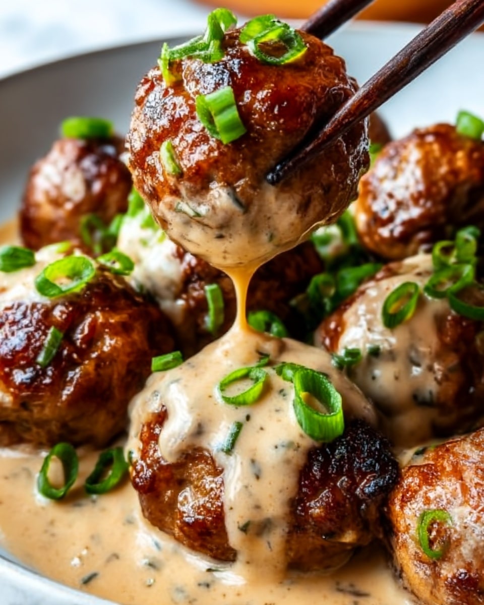 The image shows a close-up of juicy, dark brown meatballs stacked together on a white surface with a white marbled texture. A creamy, light beige sauce with black pepper flecks is generously poured over the meatballs, dripping down the sides, giving them a glossy, rich look. Fresh chopped green onions are sprinkled on top, adding a pop of green color. A pair of black chopsticks, held by a woman's hand, lifts one meatball with sauce dripping down. The texture of the meatballs is slightly crispy on the outside with a tender interior visible. photo taken with an iphone --ar 4:5 --v 7