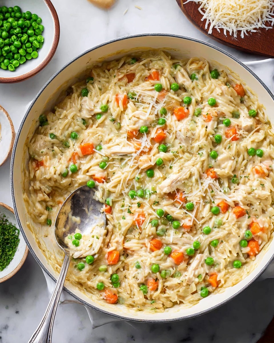 A deep white pan filled with a creamy orzo pasta mixed with small bright green peas and diced orange carrots, scattered evenly throughout. Chunks of light chicken and bits of translucent cooked onion are also mixed in, all coated in a smooth, creamy sauce giving a slightly glossy look. Some grated white cheese is sprinkled on top, melting into the pasta. A silver spoon is scooping a portion from the left side of the pan. The pan is placed on a white marbled surface, with small bowls holding more peas and shredded cheese nearby. Photo taken with an iphone --ar 4:5 --v 7