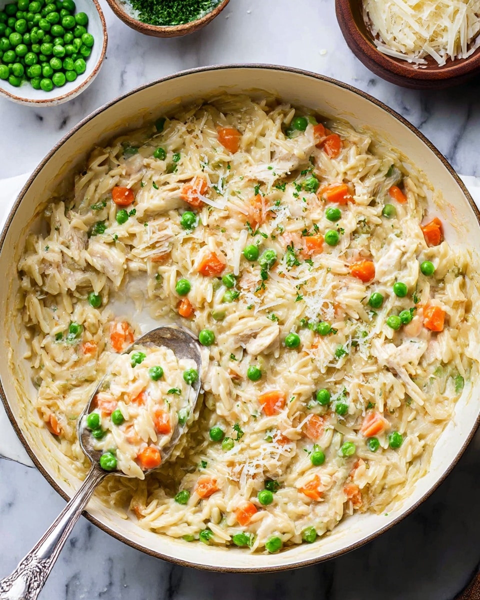 A creamy orzo dish is shown in a large white bowl with a thin dark rim, filled with three main layers: small orange carrot cubes, bright green peas, and tender shredded chicken mixed evenly throughout. The orzo pasta is soft and coated with a thick, pale yellow cream sauce that blends all ingredients together. A silver spoon is partially submerged in the bowl, lifting a generous scoop of the mixture. In the background, a small white plate holds a mound of shredded white cheese. The whole scene is set on a white marbled surface, with dark serving pieces and a small bowl of extra green peas nearby. Photo taken with an iphone --ar 4:5 --v 7