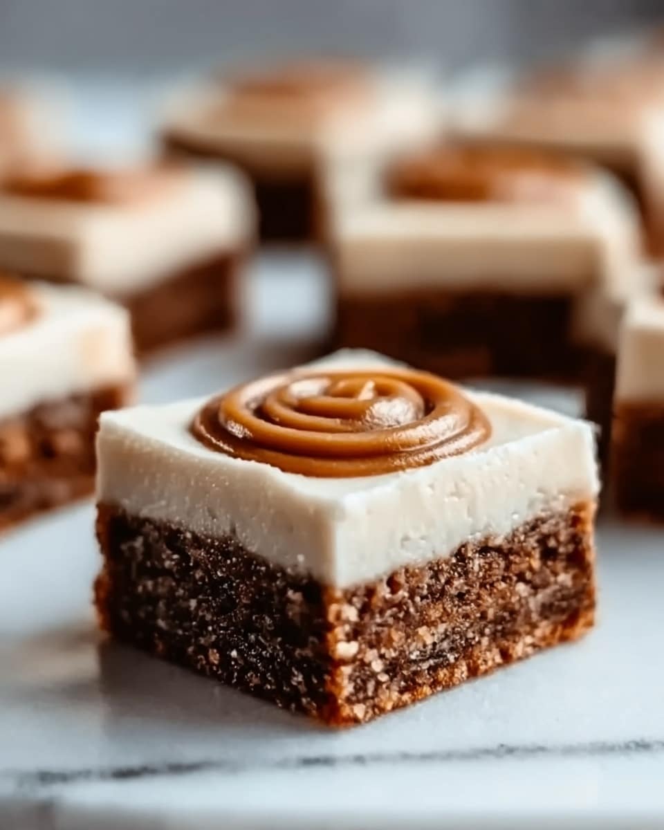 A square brownie with three clear layers sits on a white plate on a white marbled surface. The bottom layer is dark brown and looks dense and chewy, the middle layer is a creamy off-white frosting spread evenly, and the top layer is a small round swirl of caramel with a smooth texture in the center. Several similar brownies are blurred in the background. Photo taken with an iphone --ar 4:5 --v 7