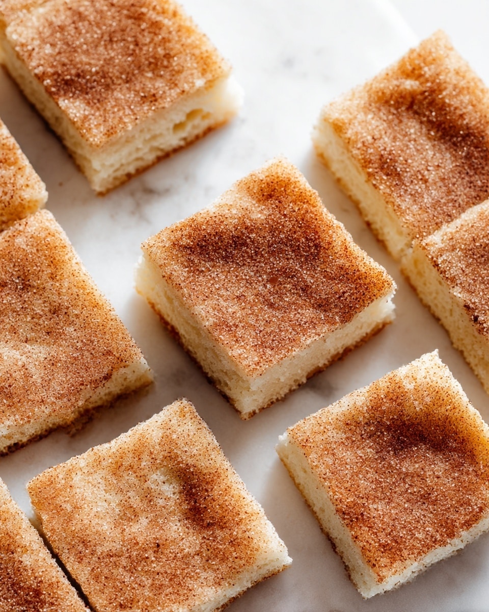 The image shows several square pieces of soft cake stacked and spread on a white marbled surface, each piece topped with a layer of cinnamon-sugar powder that looks grainy and slightly uneven. The cake layers appear fluffy and light tan colored with a slightly coarse texture visible inside. Some cake pieces are sliced but still touching, and one piece is in focus at the front center, showing a gentle rise and soft crumb. The background is blurred white marbled texture that contrasts the warm brown of the cinnamon topping. Photo taken with an iphone --ar 4:5 --v 7