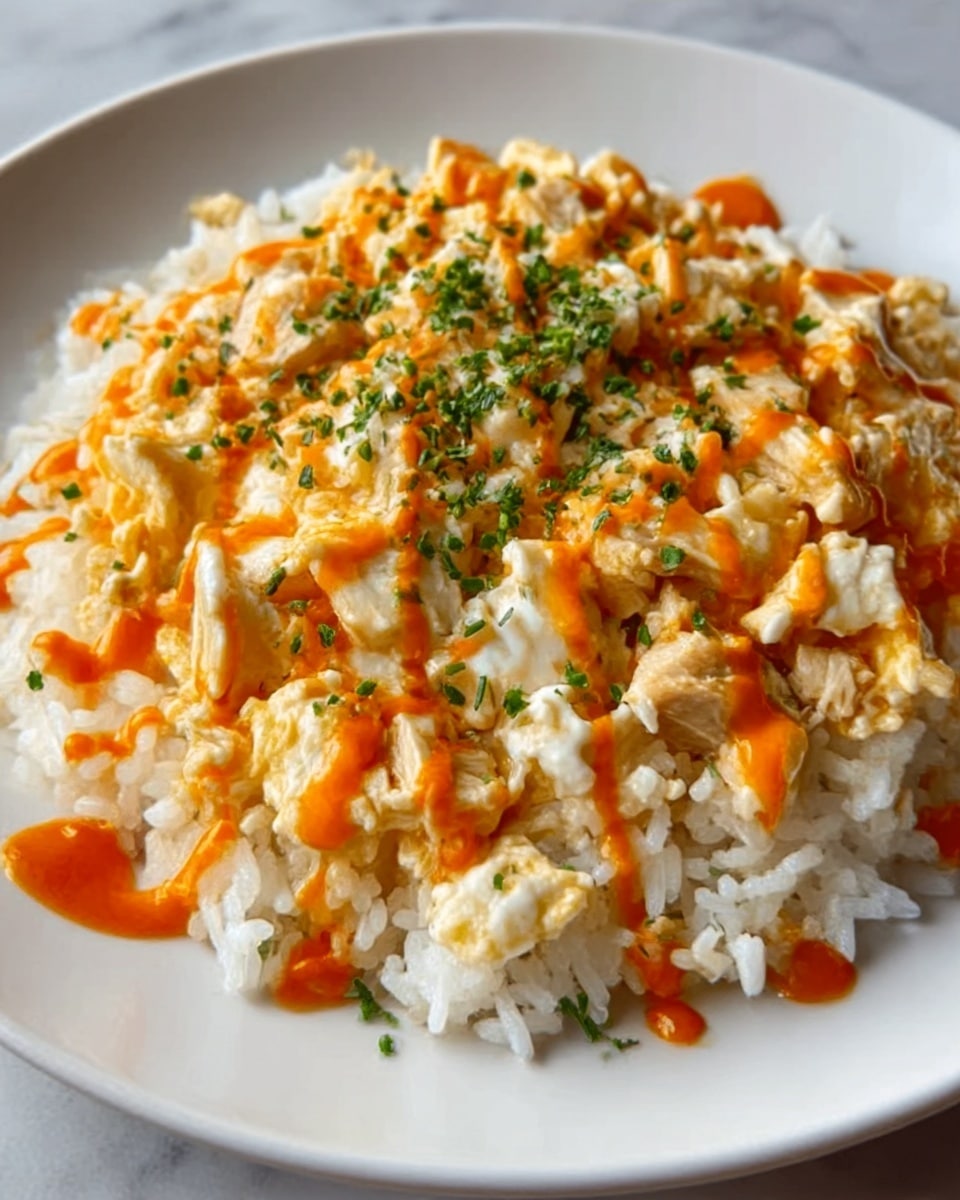 The image shows a white plate with a base layer of cooked white rice topped with scrambled eggs mixed with small pieces of chicken. Bright orange hot sauce is drizzled in thin lines over the eggs and rice. Sprinkles of chopped green herbs add a fresh touch on top. The white marbled surface beneath the plate adds a clean, bright background. Photo taken with an iphone --ar 4:5 --v 7