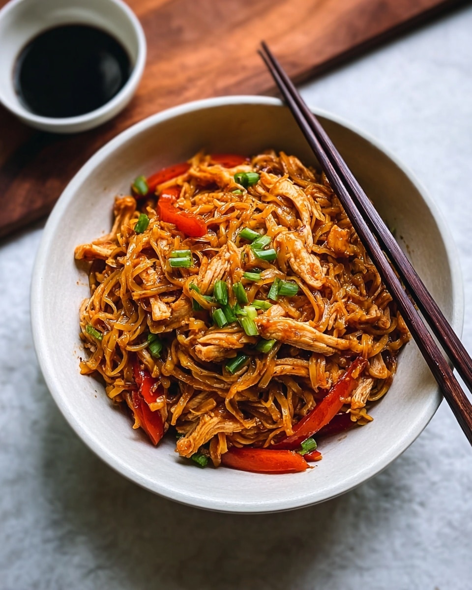 A white bowl filled with savory noodles mixed with strips of cooked chicken and thin slices of red bell pepper, all coated in a glossy brown sauce. The noodles look soft and slightly curled, scattered with chopped green onions on top for a fresh pop of color. Two dark brown chopsticks rest diagonally on the rim of the bowl. Nearby, there is a small white bowl of dark soy sauce placed on a white marbled surface. Photo taken with an iphone --ar 4:5 --v 7
