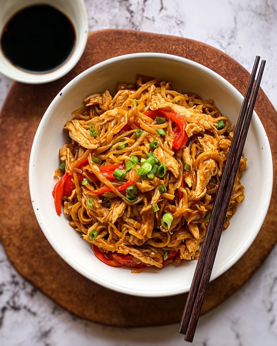 A bowl with three main layers shows a dish of stir-fried noodles on a white marbled textured surface. The bottom layer is a wide, white bowl with a slightly speckled texture and rimmed with a rougher beige edge. Inside is a heap of stir-fried noodles, colored light brown and soaked in glossy sauce, mixed with small pieces of light tan chicken, vibrant red bell pepper strips, and bits of green onion on top. Resting across the bowl are two dark brown wooden chopsticks. In the background, there is a small white bowl filled with dark soy sauce. Photo taken with an iphone --ar 4:5 --v 7
